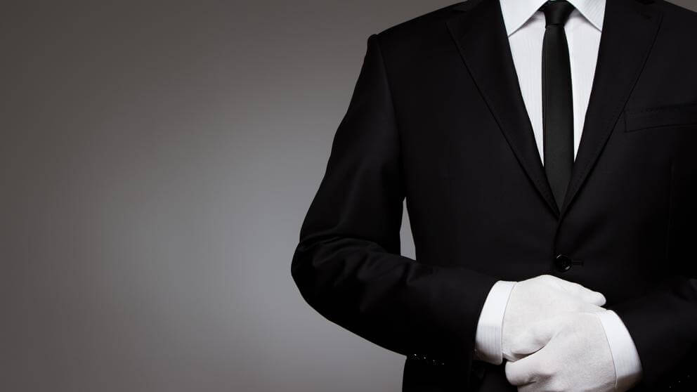 Concierge in a dark suit and white gloves standing with hands clasped
